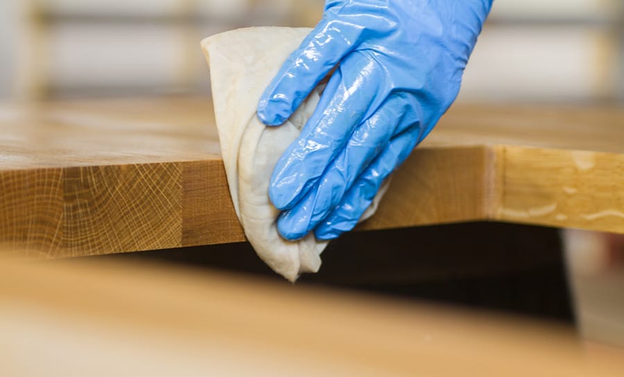 Gloved hand applying oil to the edge of an oak worktop with a cloth