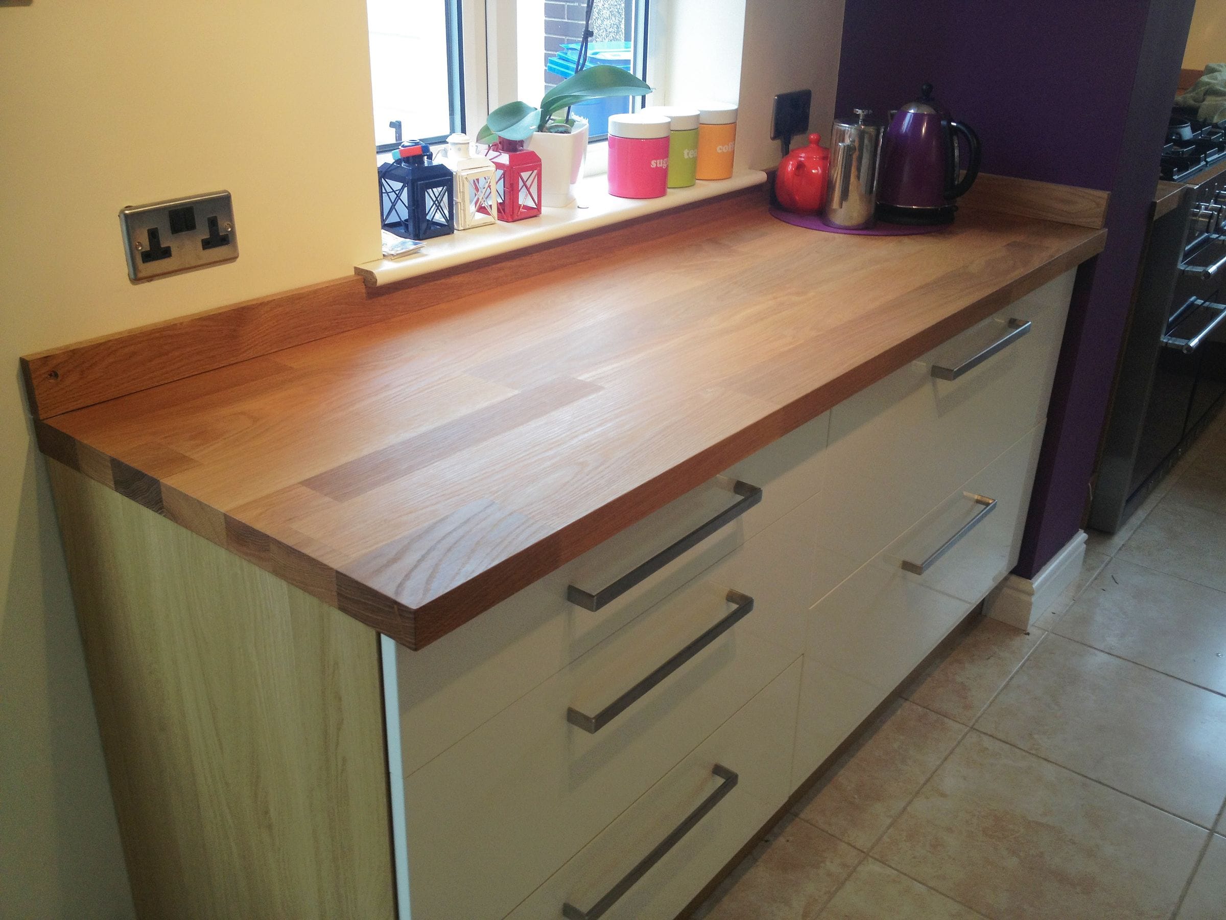 Oak worktop and upstand on white drawer units with kettle and tea canisters