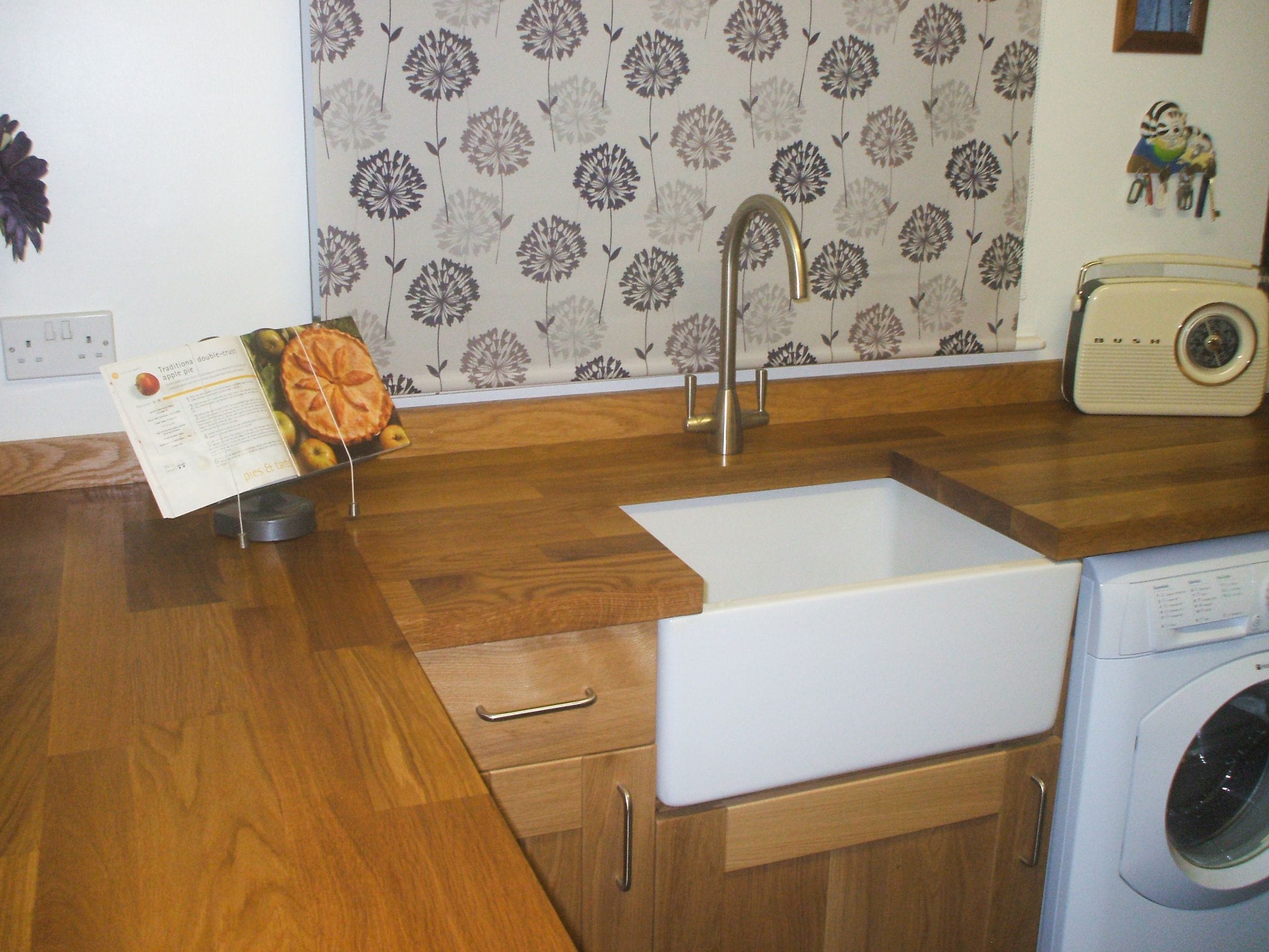 Oak worktop around a Belfast sink with retro radio and floral blind