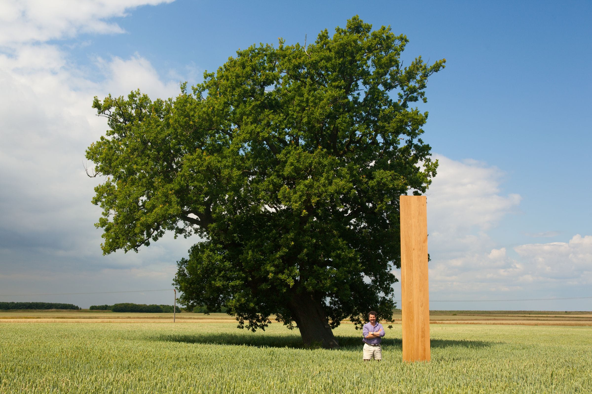 Man standing with an upright oak worktop beside a mature oak tree in a field