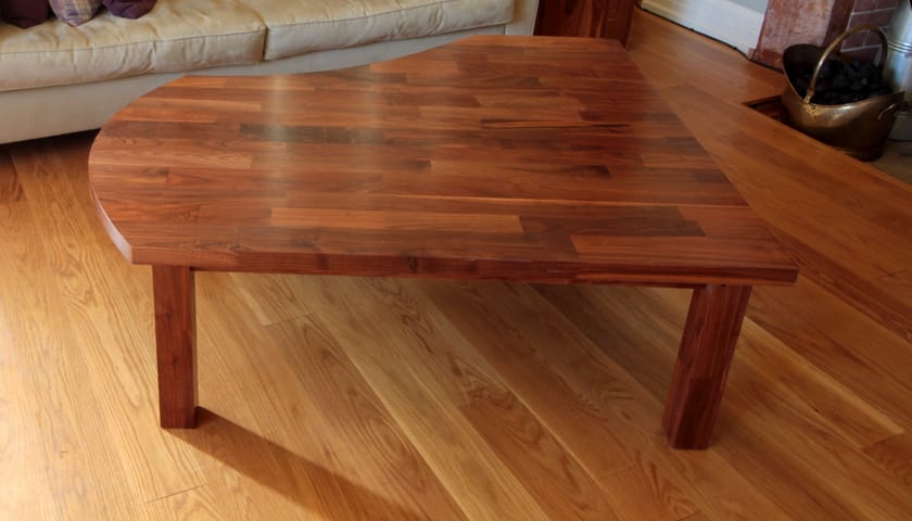 Curved bespoke walnut coffee table on oak flooring beside a fireplace