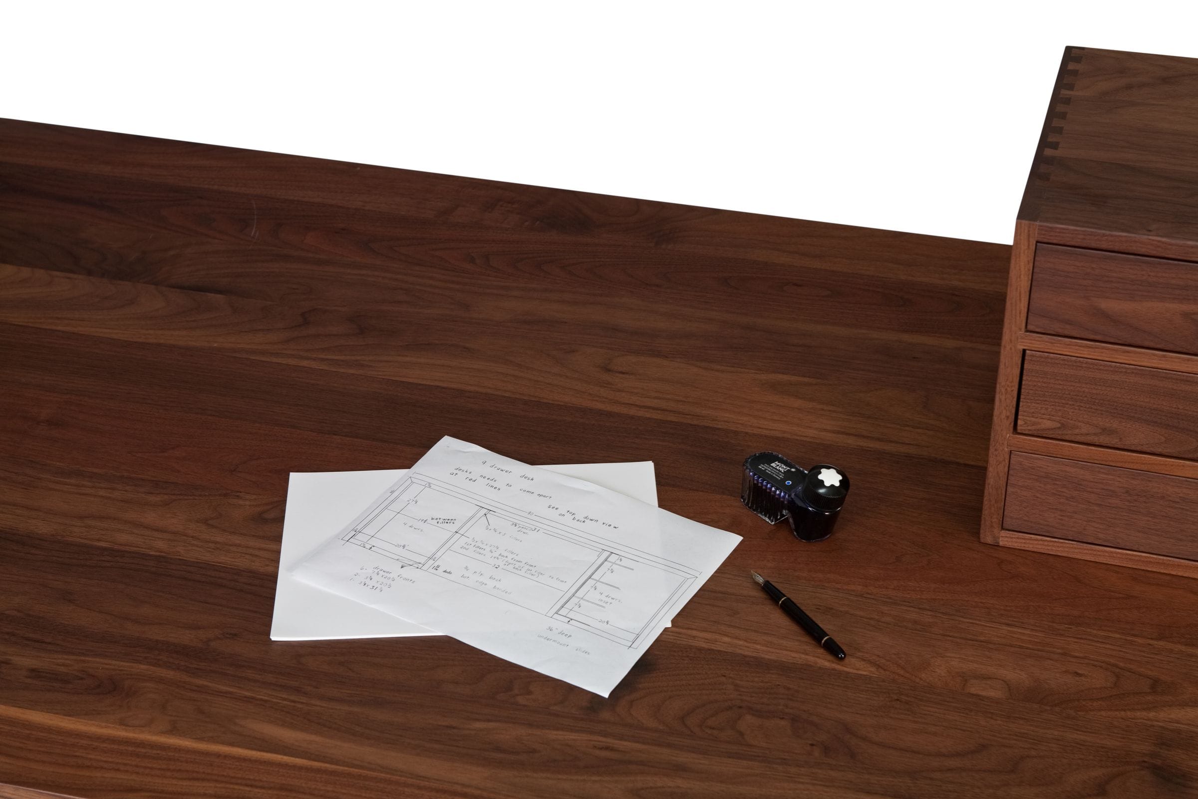 Walnut desktop with hand-drawn plans, fountain pen and ink bottle