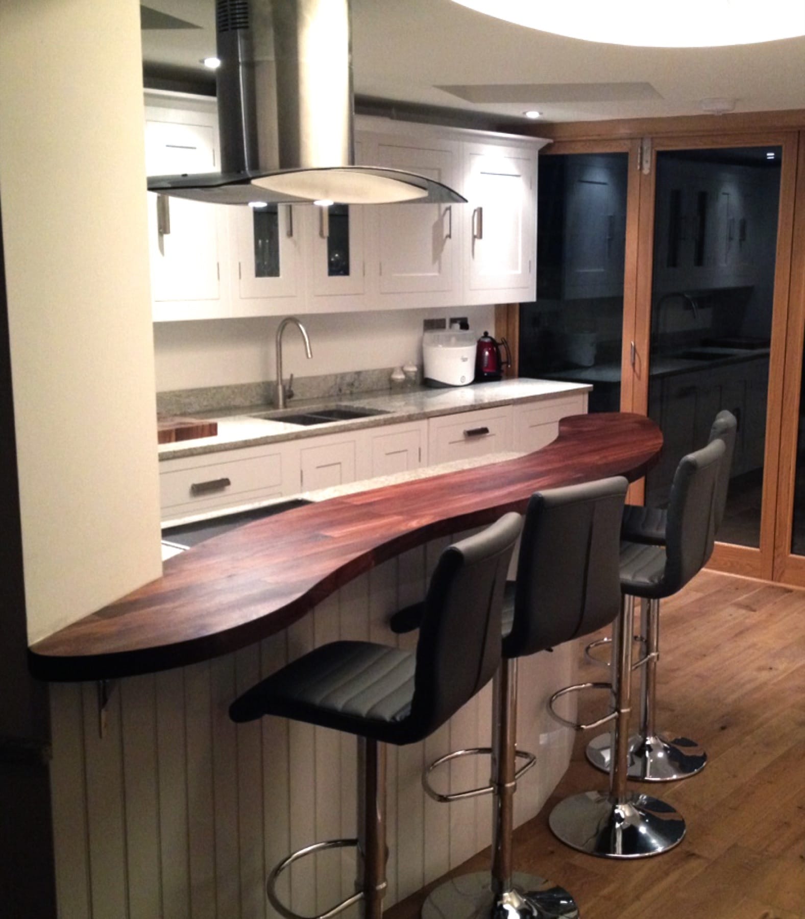 Curved walnut breakfast bar with grey bar stools beside a granite-topped kitchen