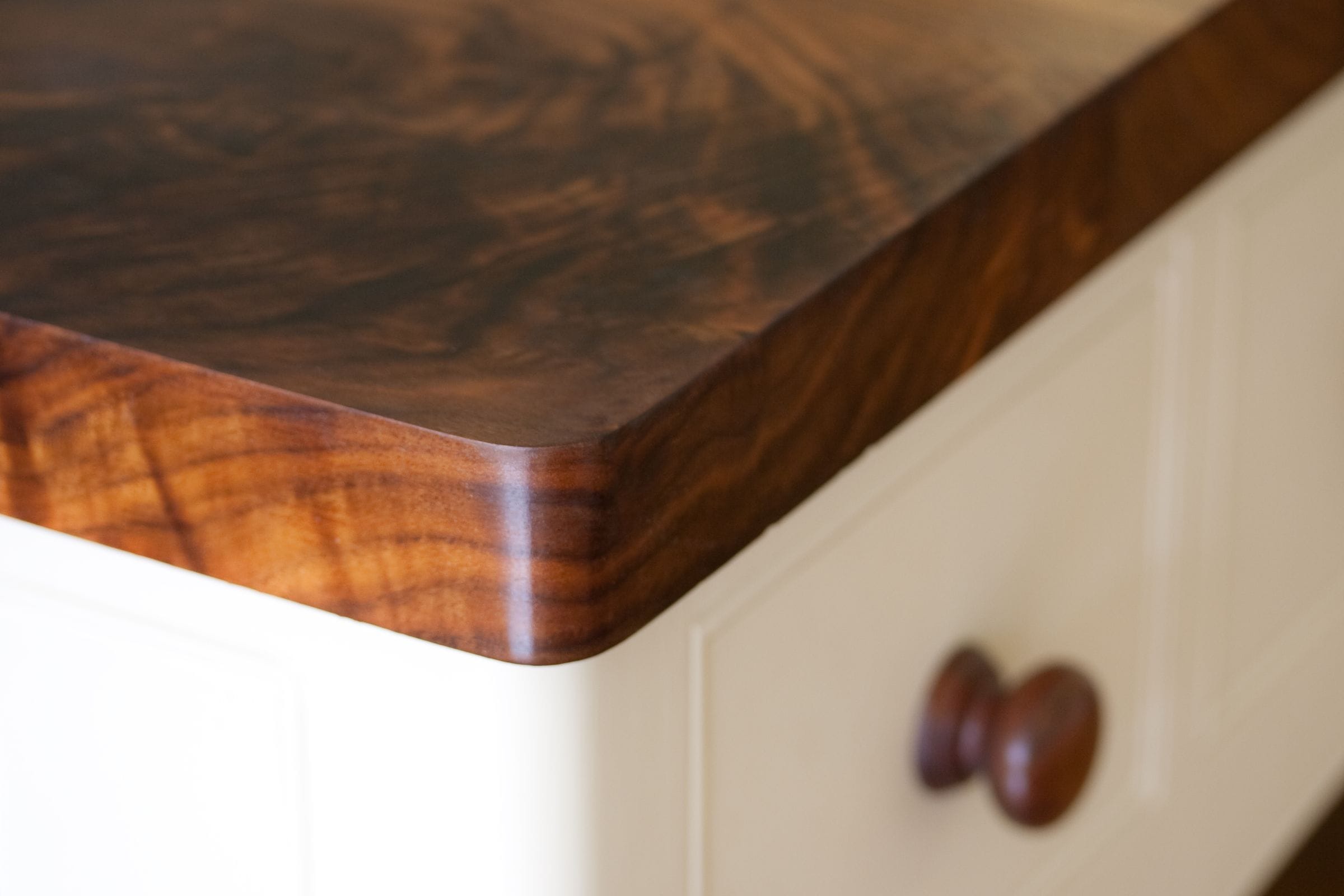 Corner detail of figured walnut worktop with rounded edge on cream cabinetry