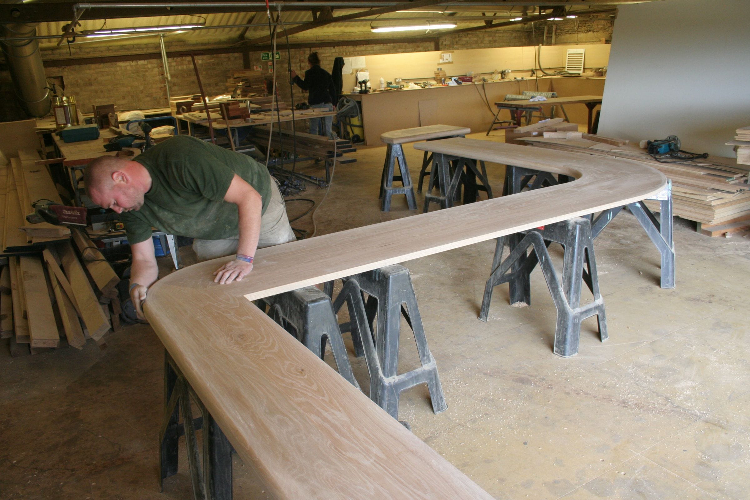 Craftsman hand-finishing a long curved worktop on trestles in the workshop