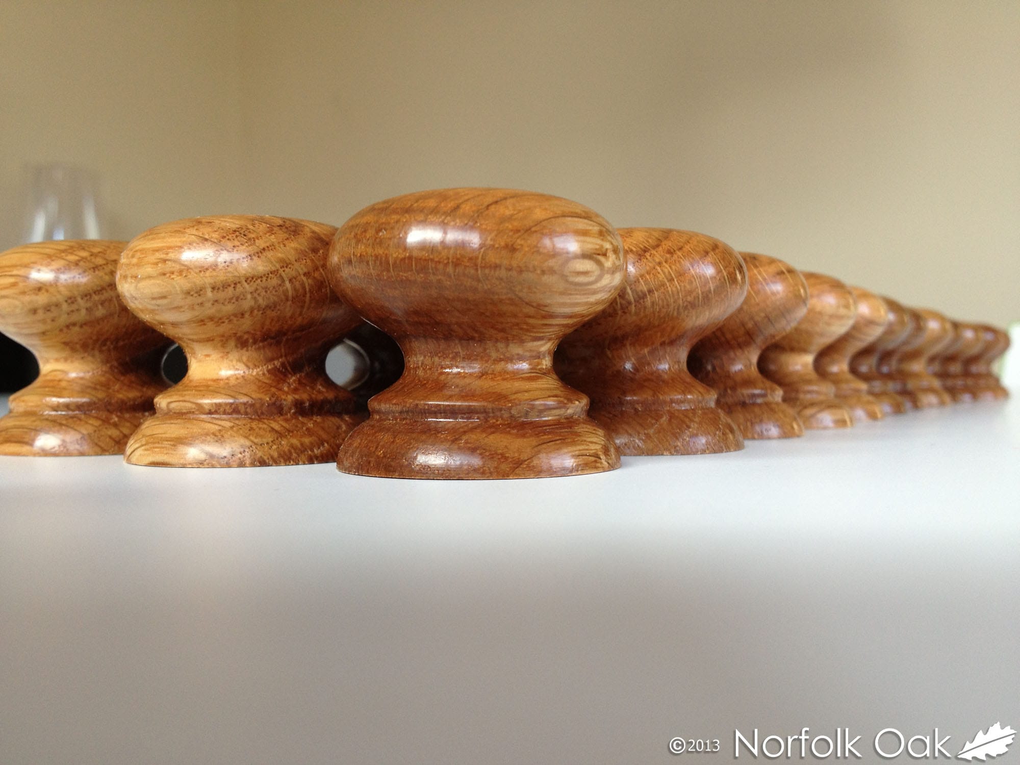 Row of hand turned oak cabinet knobs lined up on a white surface