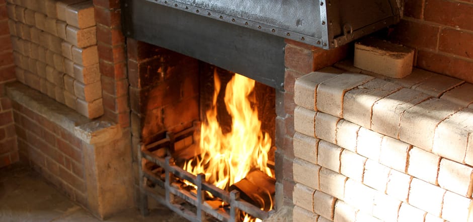 Wood briquettes stacked beside an open brick fireplace with a roaring fire