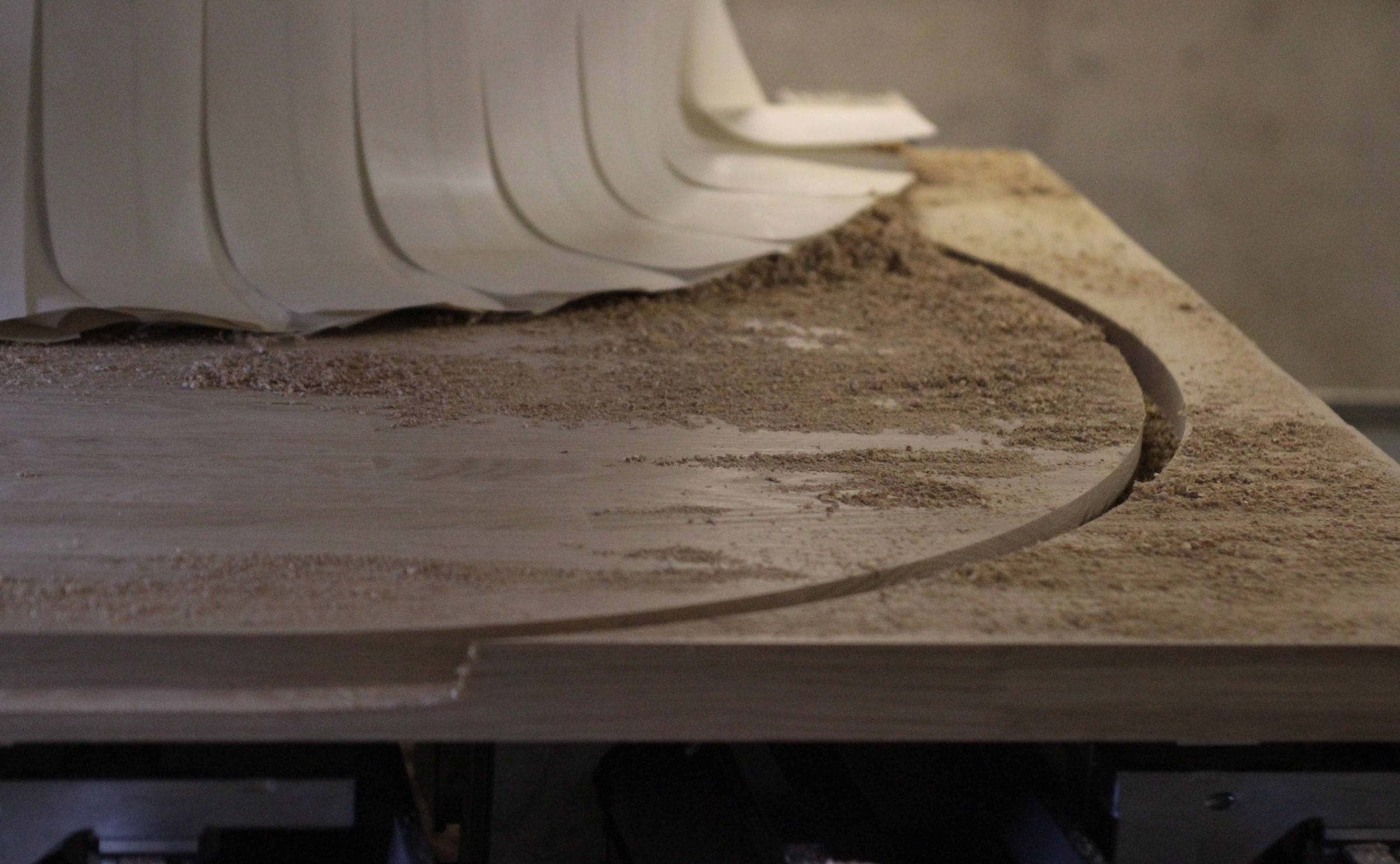 CNC machine cutting a curved edge into an oak worktop, shavings on the surface