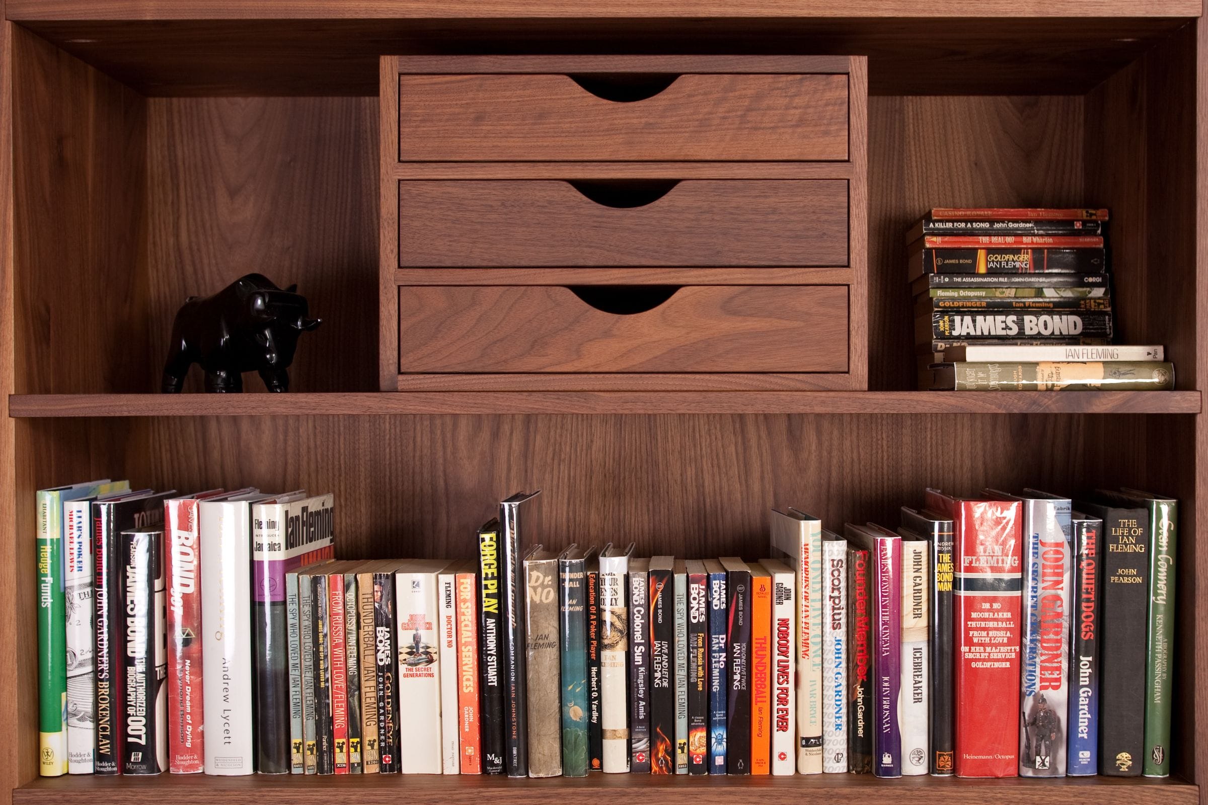 Walnut bookshelf with built-in drawers holding rows of paperback books