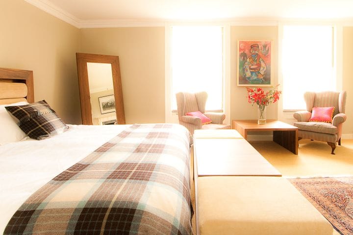 Bright bedroom with tartan throw on the bed, armchairs and a freestanding mirror