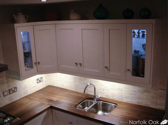 Dark walnut worktop and stainless steel sink beneath illuminated cream cabinets