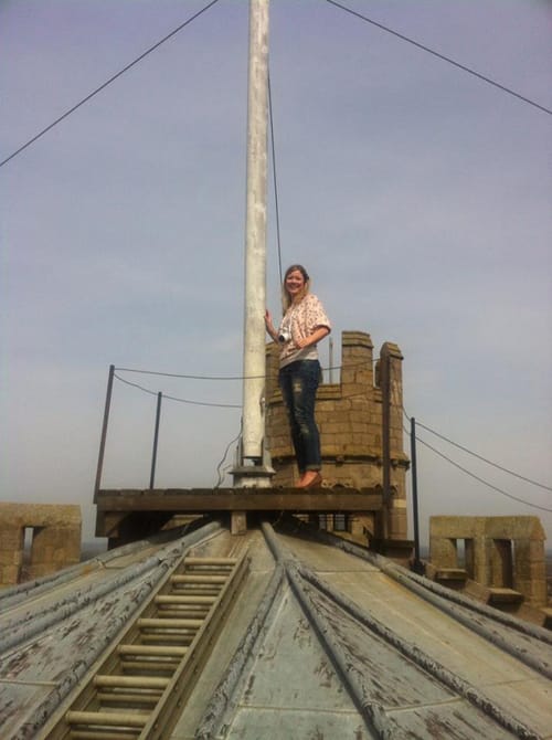 Woman standing beside a flagpole on the leaded rooftop of a historic stone tower