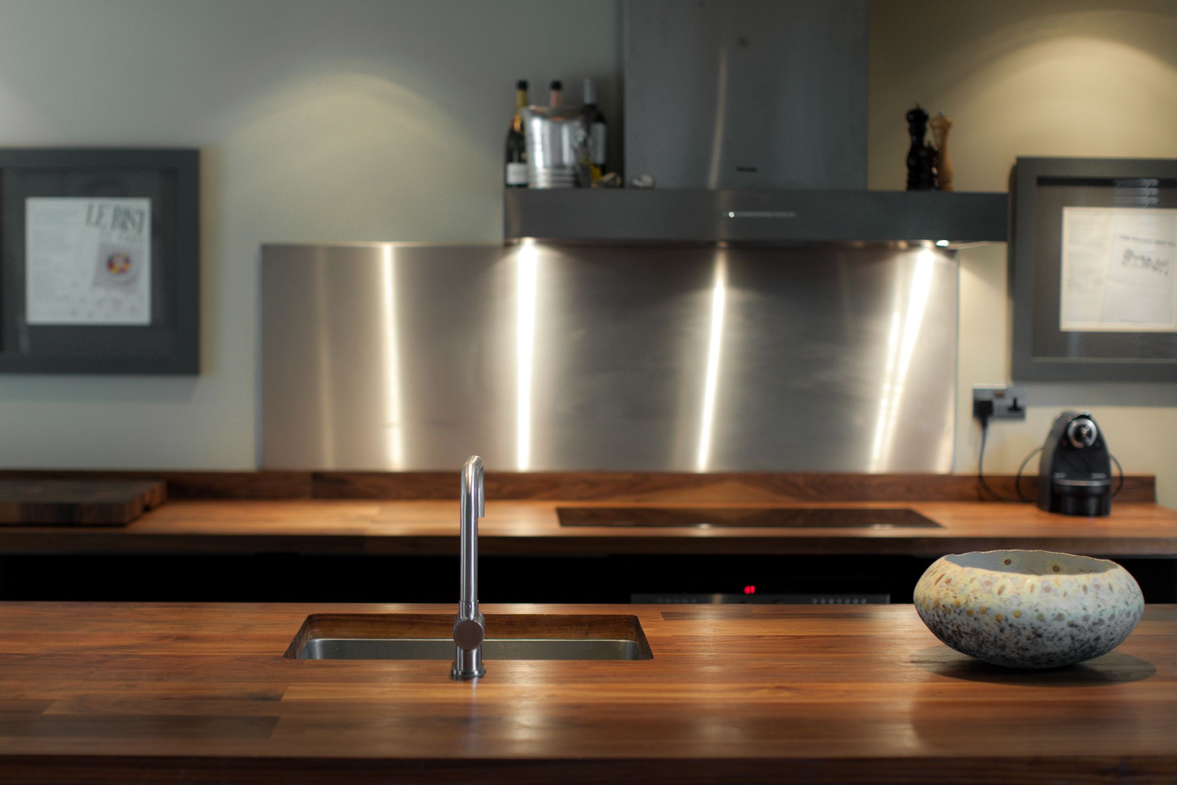 Walnut plank worktop island with inset sink facing a stainless steel splashback