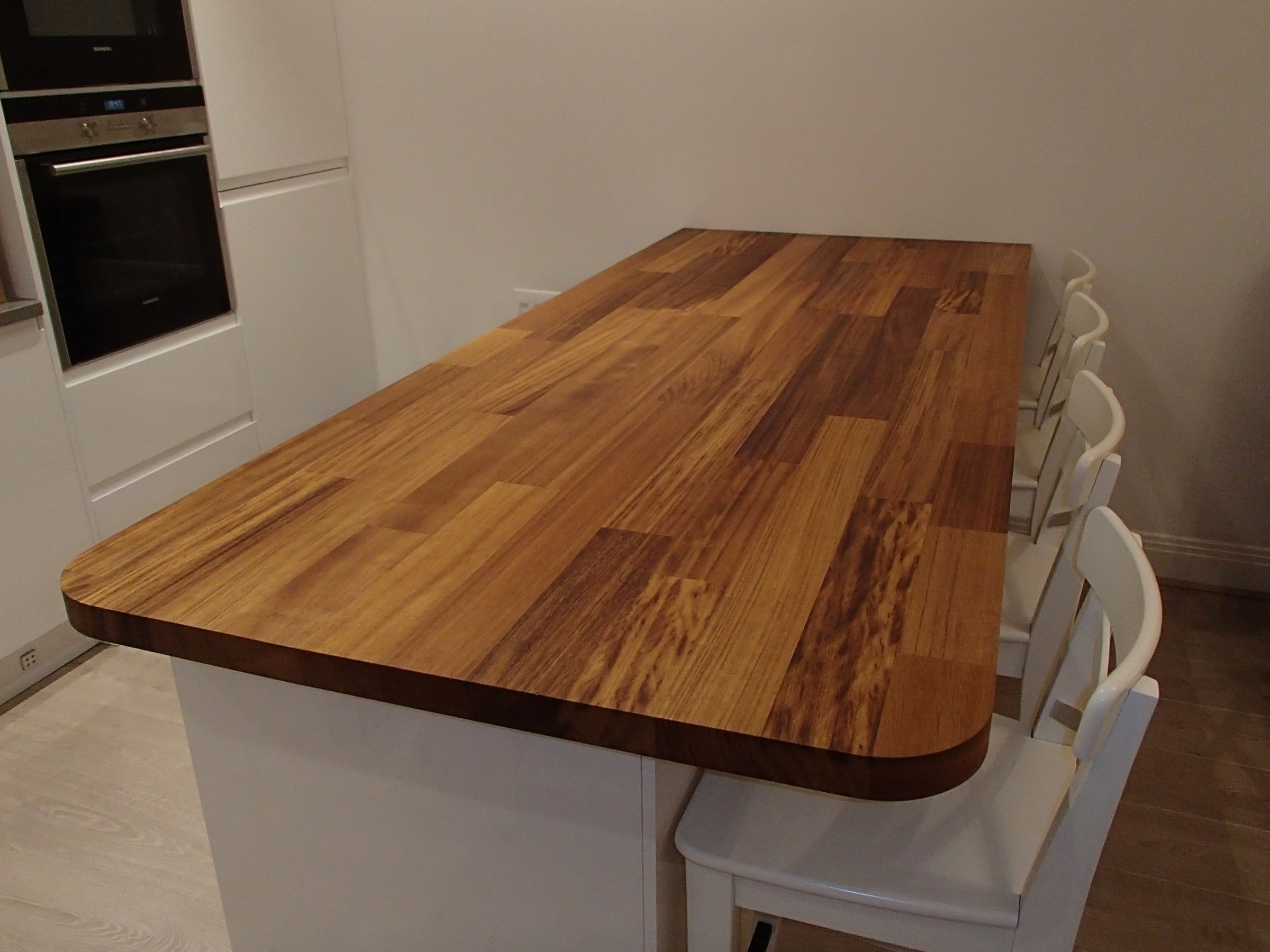 Iroko breakfast bar with rounded corners and white bar stools in a modern kitchen