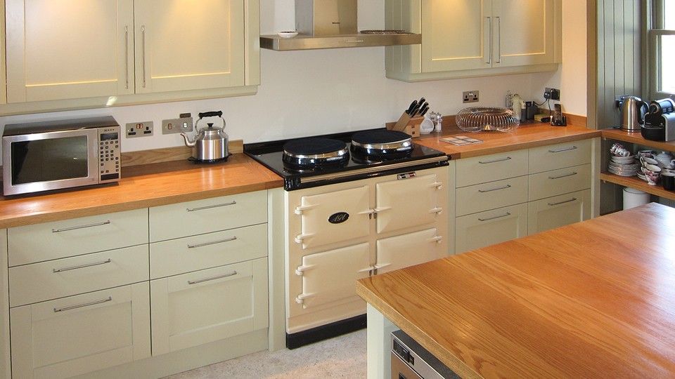 Sage green shaker kitchen with oak worktops and a cream Aga