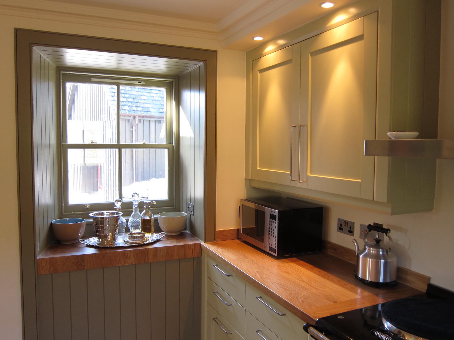 Country kitchen with oak worktops, sage-green panelling and cream cabinets