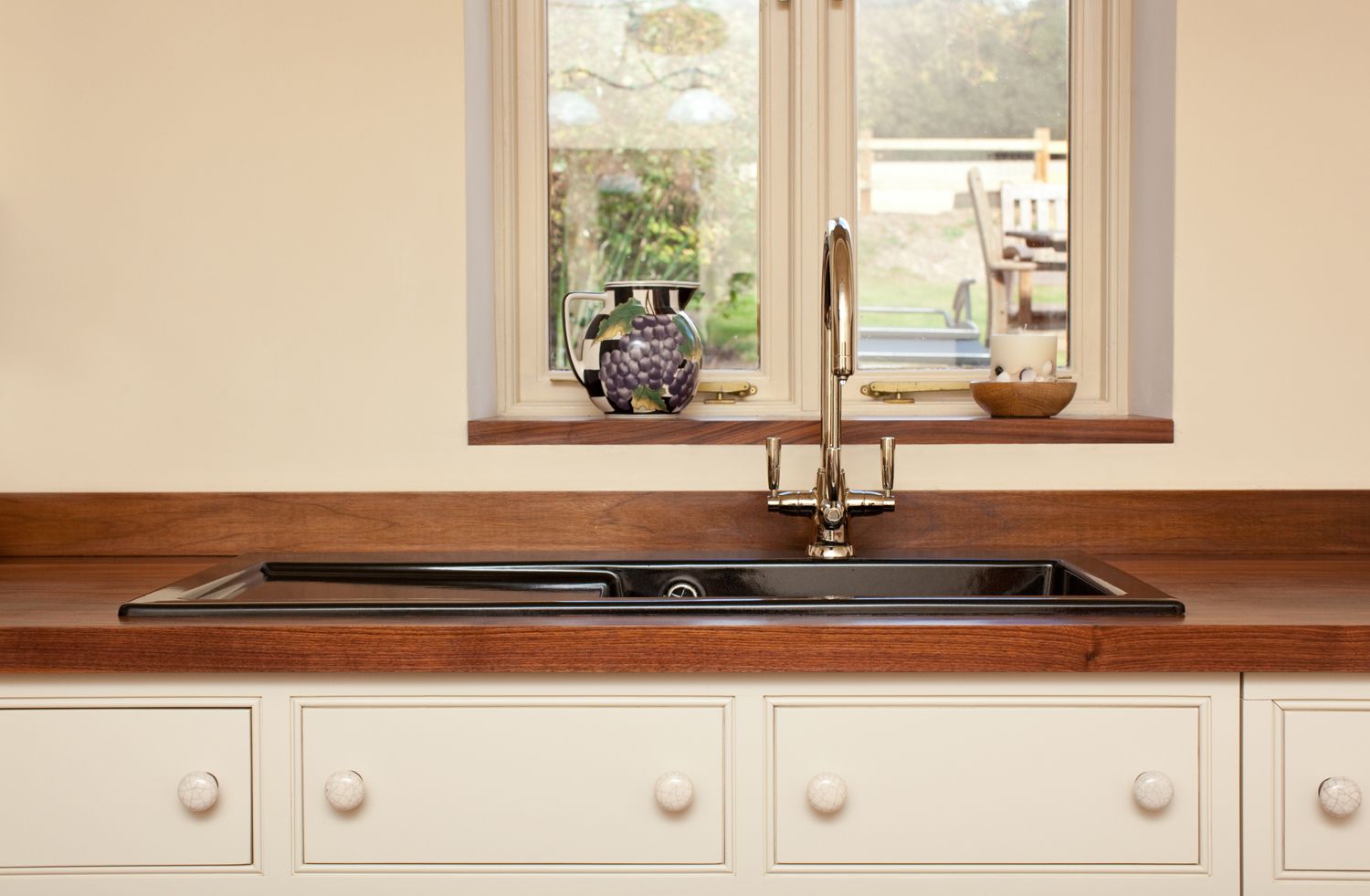 Walnut worktop with inset black sink and chrome tap beneath a cottage window