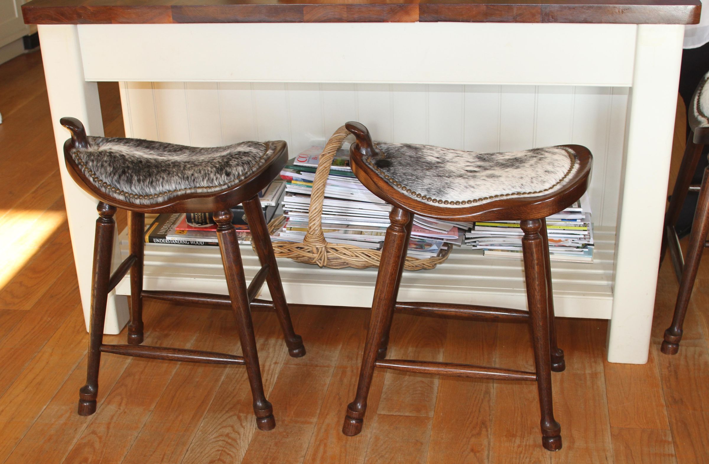 Western Oak Stool Two oak saddle stools with studded cowhide seats beside a cream kitchen island