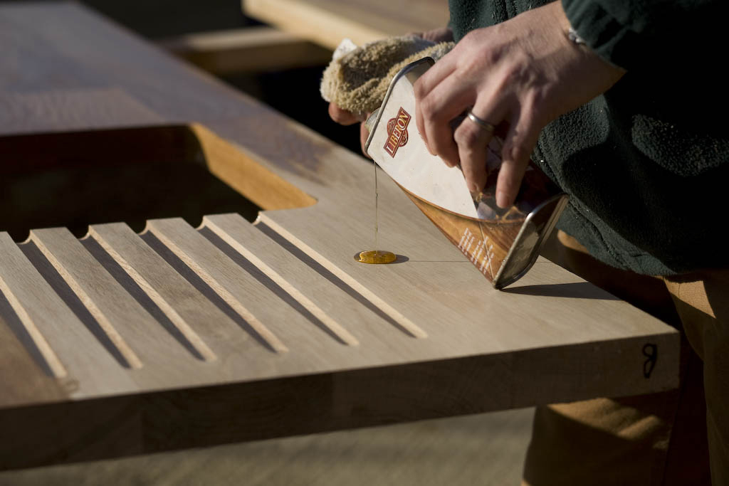 worktop-sealing Tung oil poured from a tin onto an oak draining board section outdoors
