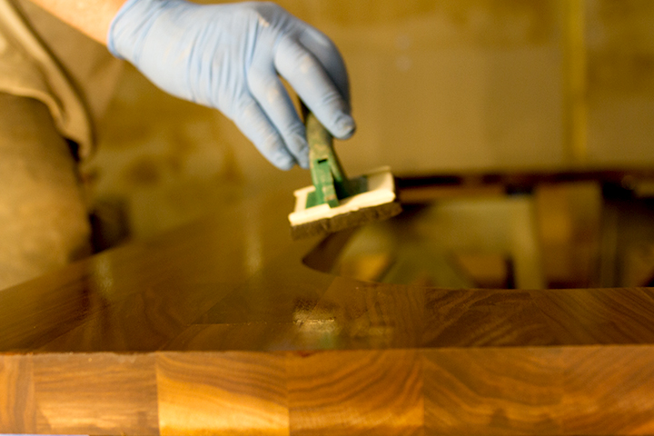 worktop oiling technology Gloved hand applying protective oil to a dark walnut worktop with an applicator pad