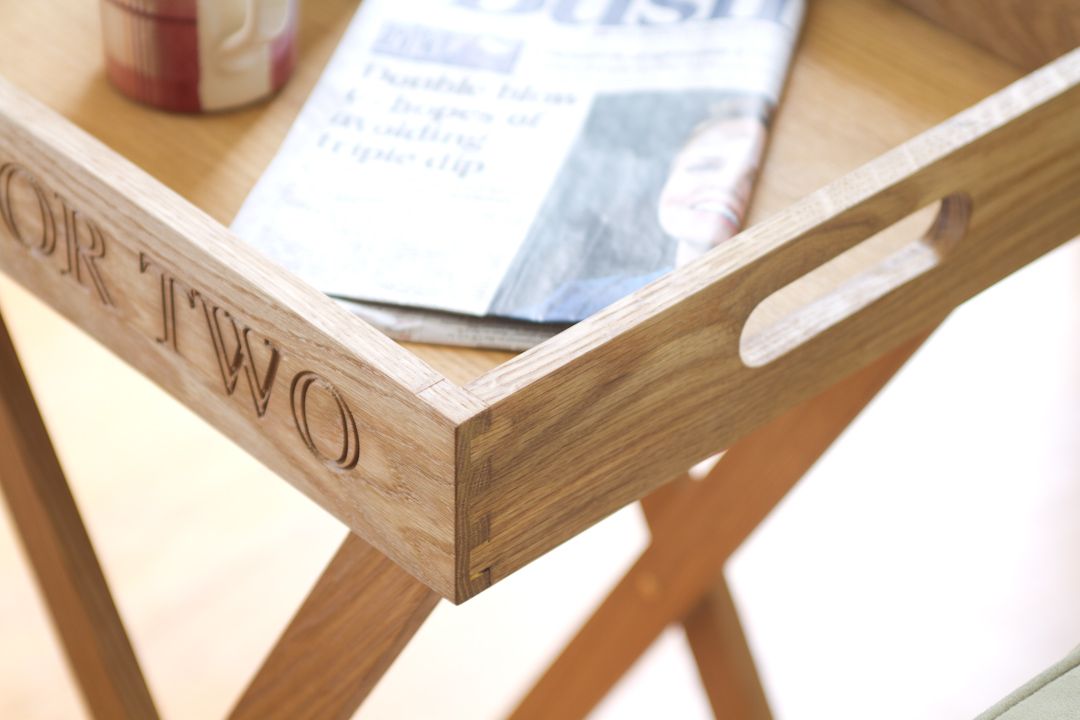 Corner of an engraved oak butler's tray holding a newspaper, showing dovetail joints