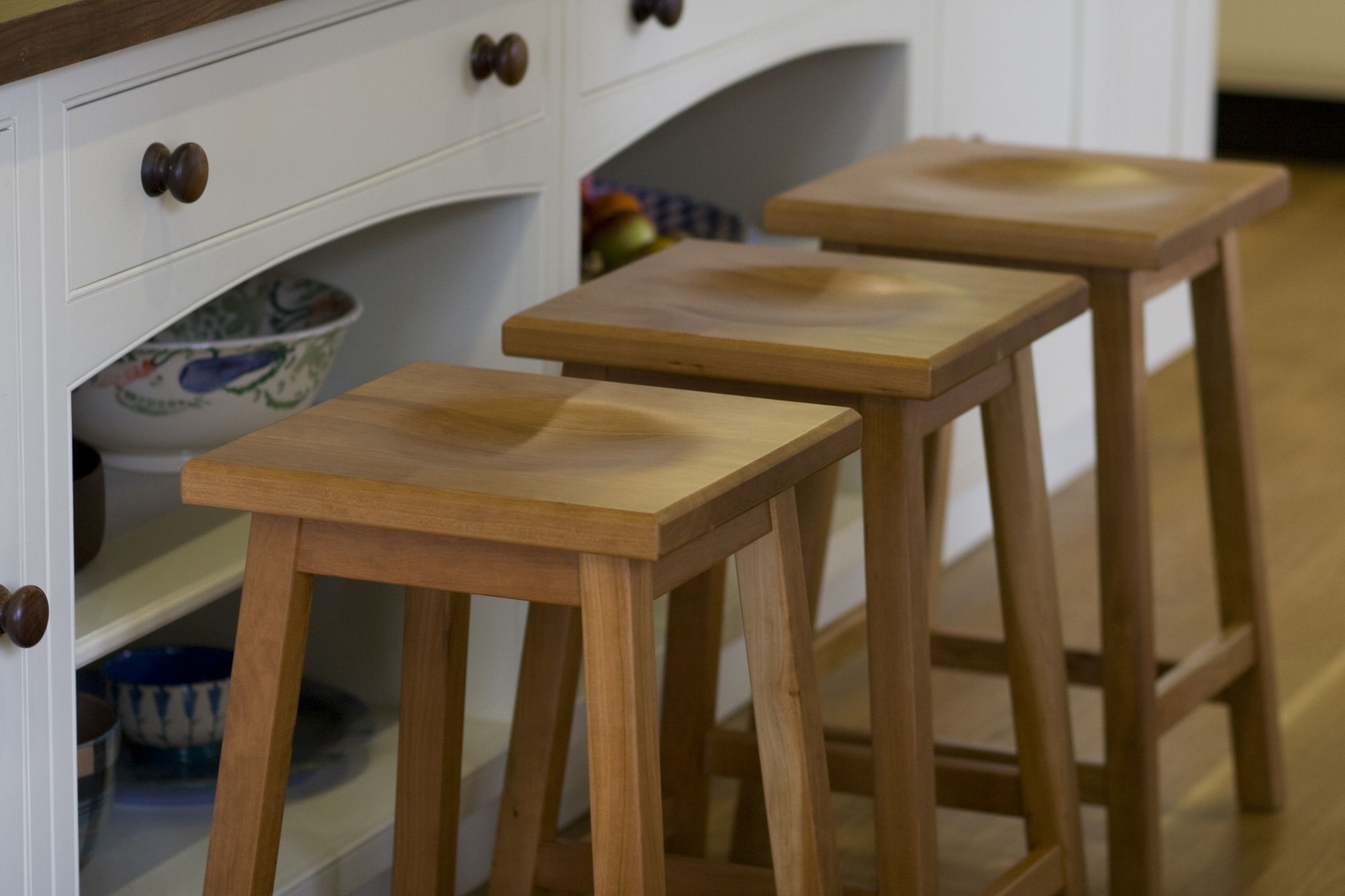 Three oak kitchen stools with scooped seats lined up along a white dresser