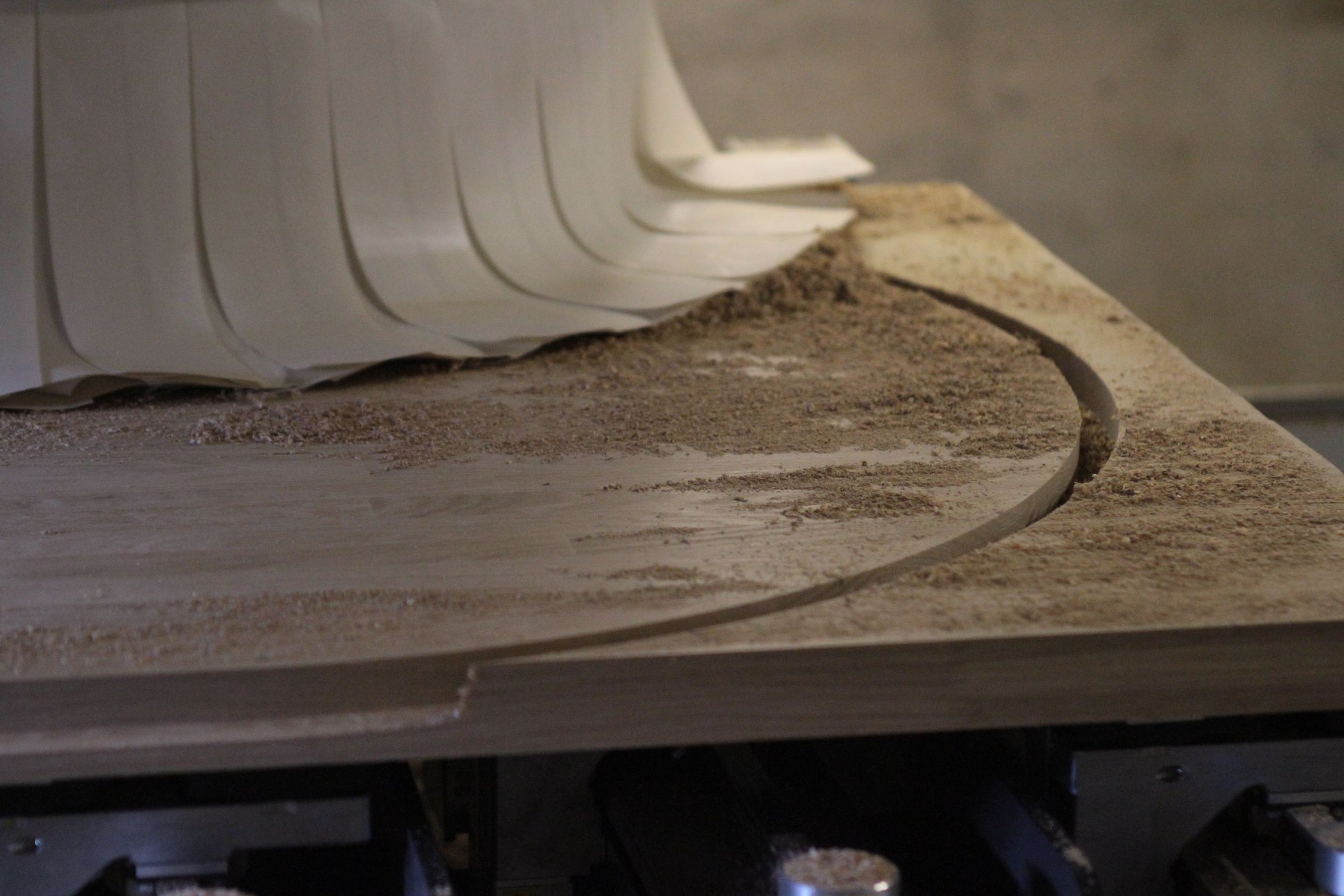 Curved cut-out being CNC machined into a wooden worktop, sawdust on the surface