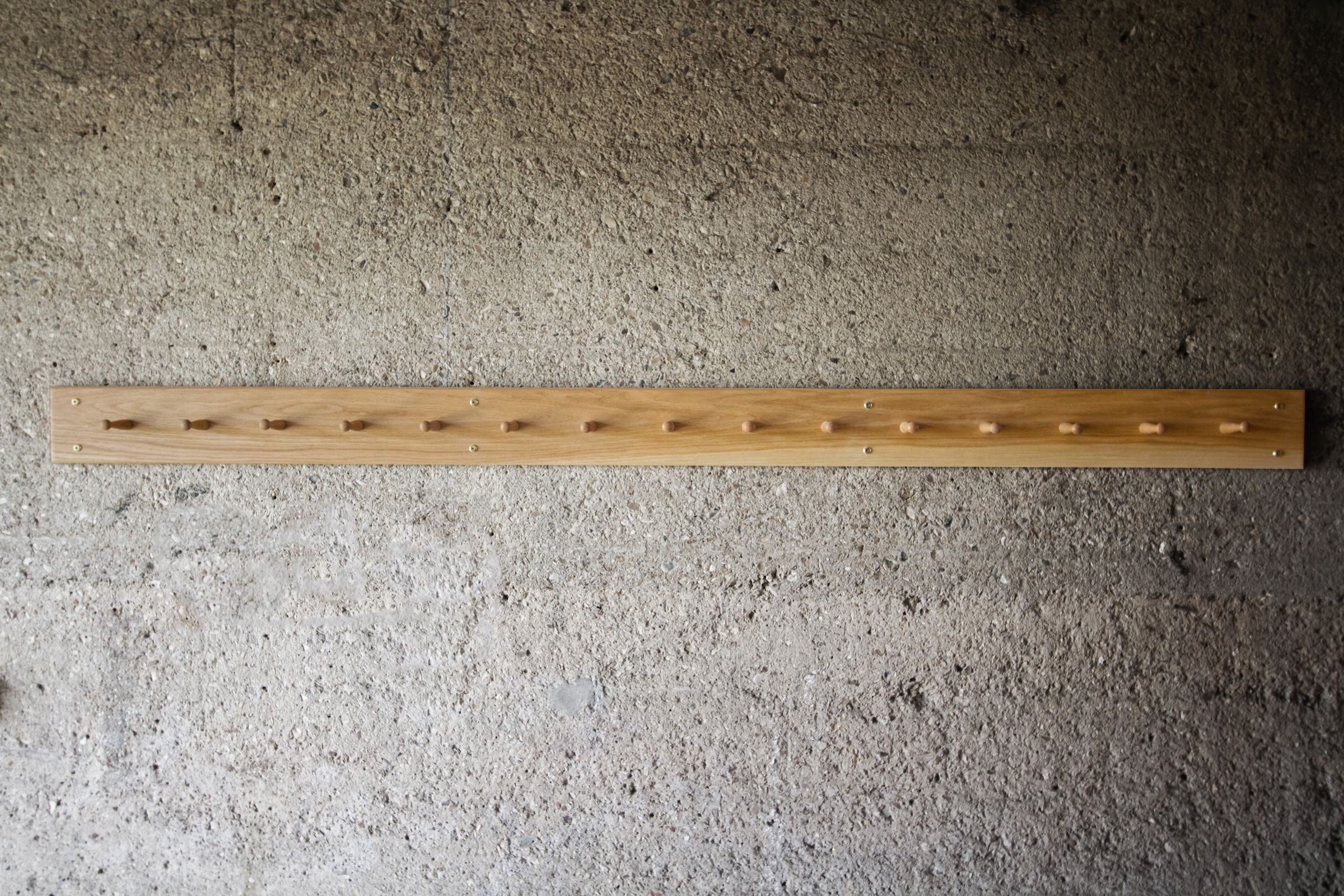 Extra-long oak Shaker peg rail with fifteen pegs mounted on a concrete wall