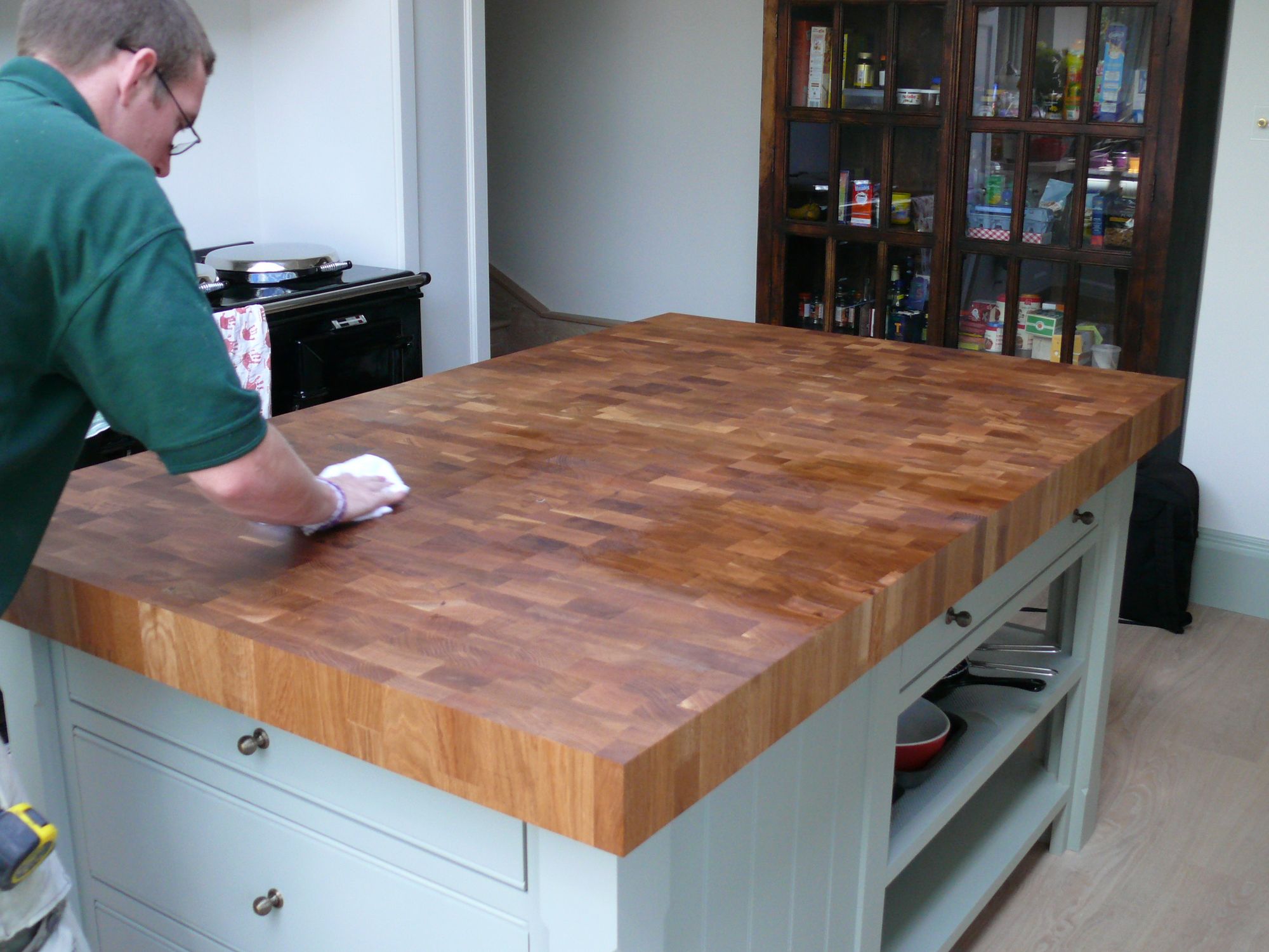 Fitter wiping down an end grain oak island worktop in a pale green kitchen
