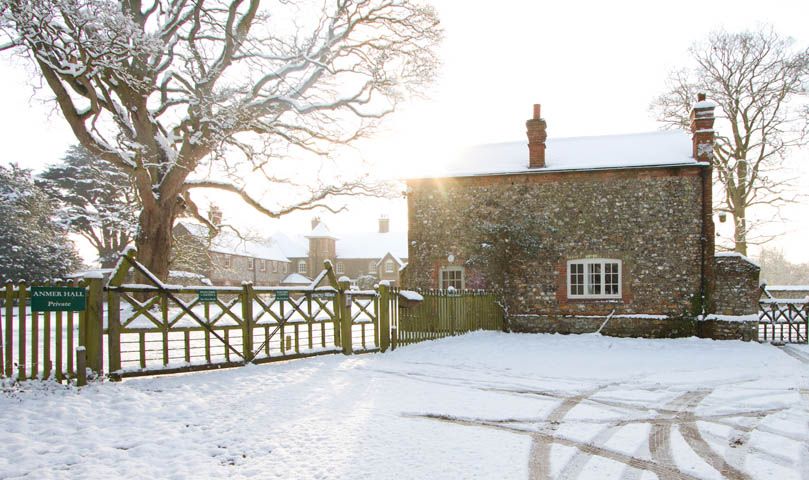 Snowy flint cottage and gated entrance at Anmer Hall in low winter sun
