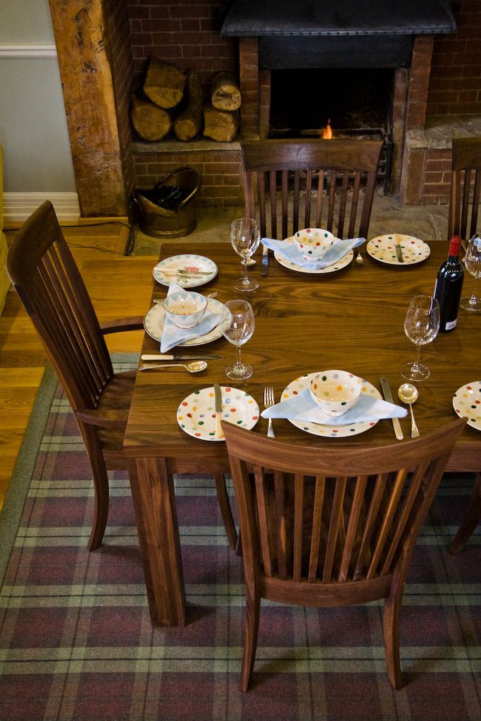 Walnut dining table and chairs laid for dinner beside an open log fire