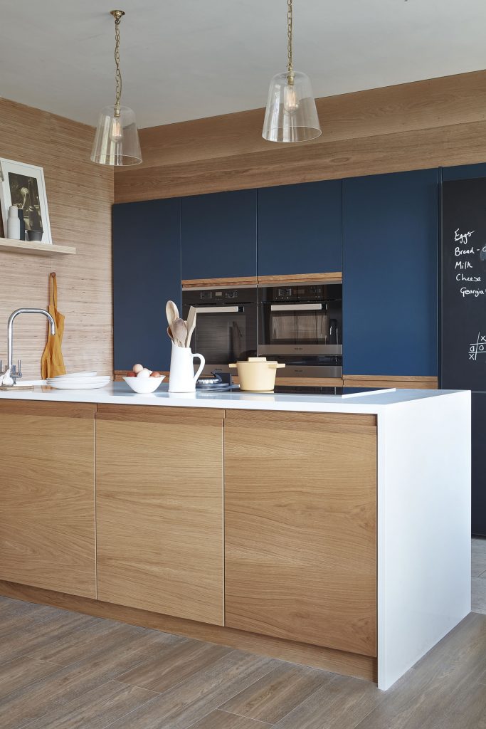 Oak kitchen island with white worktop against deep blue cabinets and a chalkboard wall