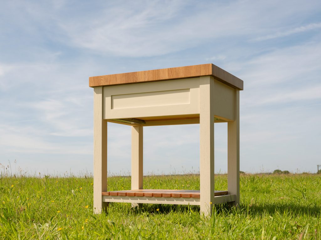 Cream-painted bespoke butcher's block with oak top and slatted shelf, photographed in a meadow
