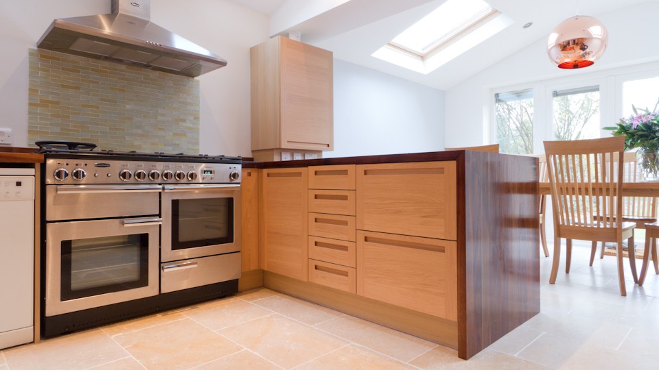 Kitchen island with oak drawers and walnut end panels beside a stainless range cooker